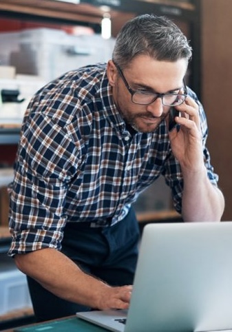 Warehouse owner taking orders over the phone while working on a laptop